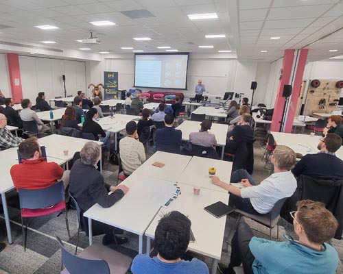 Photo showing a room of people seated around tables watching a presentation at the prosquared launch event