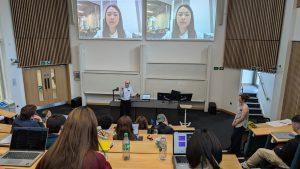 Mandy Xiang appears on two large screens in a crowded lecture theatre as she speaks remotely to the audience.