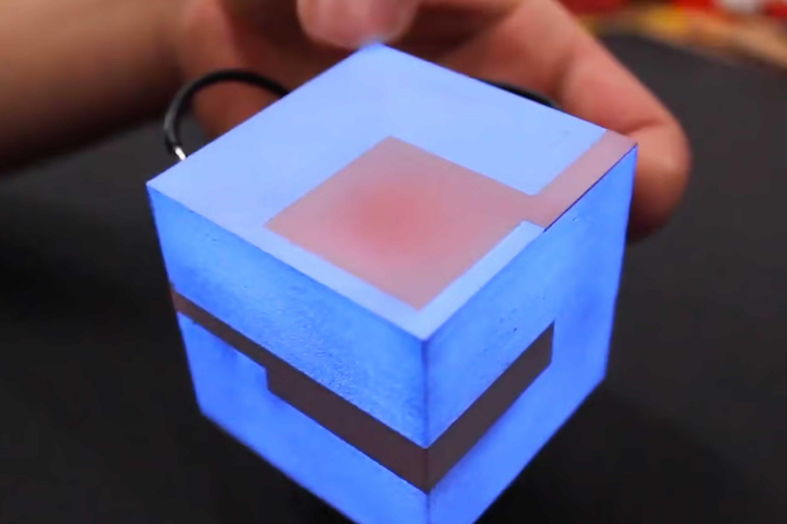 A close-up photo of a glowing blue cube with geometric patterns, which a person's hand is touching.