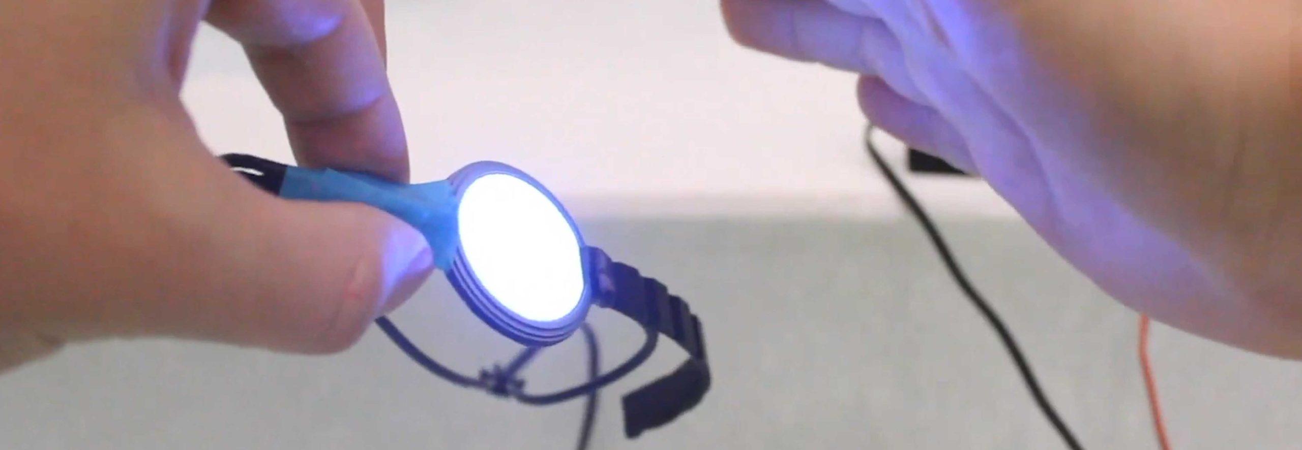 A person's hands holding a wearable electronic band, part of which is glowing white.