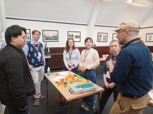 Attendees at a Pre-CHI workshop stand around a table, which is covered in crafting supplies like paper, Play-Doh, and Legos.