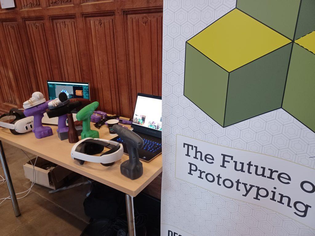 A table at the pre-CHI event holds VR headsets, 3D printed prototypes of electric drills, and two laptops. To the right a large white banner reads 'The Future of Prototyping'.