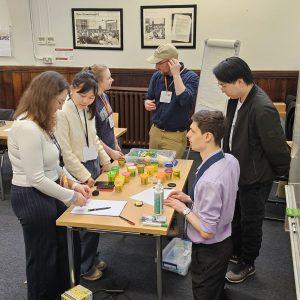 Attendees at a Pre-CHI workshop stand around a table, which is covered in crafting supplies like paper, Play-Doh, and Legos.