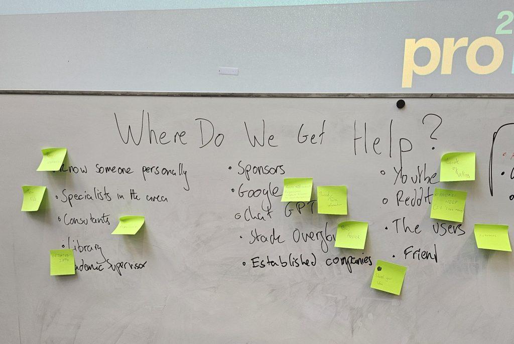 Handwritten text on a white board displays responses to the question 'where do we get help?' Light green Post-It notes are stuck next to some responses.