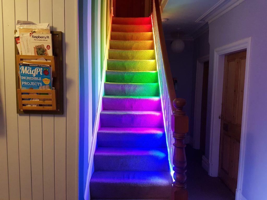 A photo displays a set of stairs in a home lit up with rainbow coloured LEDs.