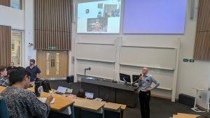 Steve Hodges speaks into a microphone in a crowded lecture theatre. On a large screen presenter Mandy Xiang can be seen addressing the crowd.
