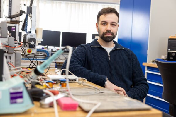 A photo of Oktay Cetinkaya sitting in a lab, with equipment on the desk in the foreground.
